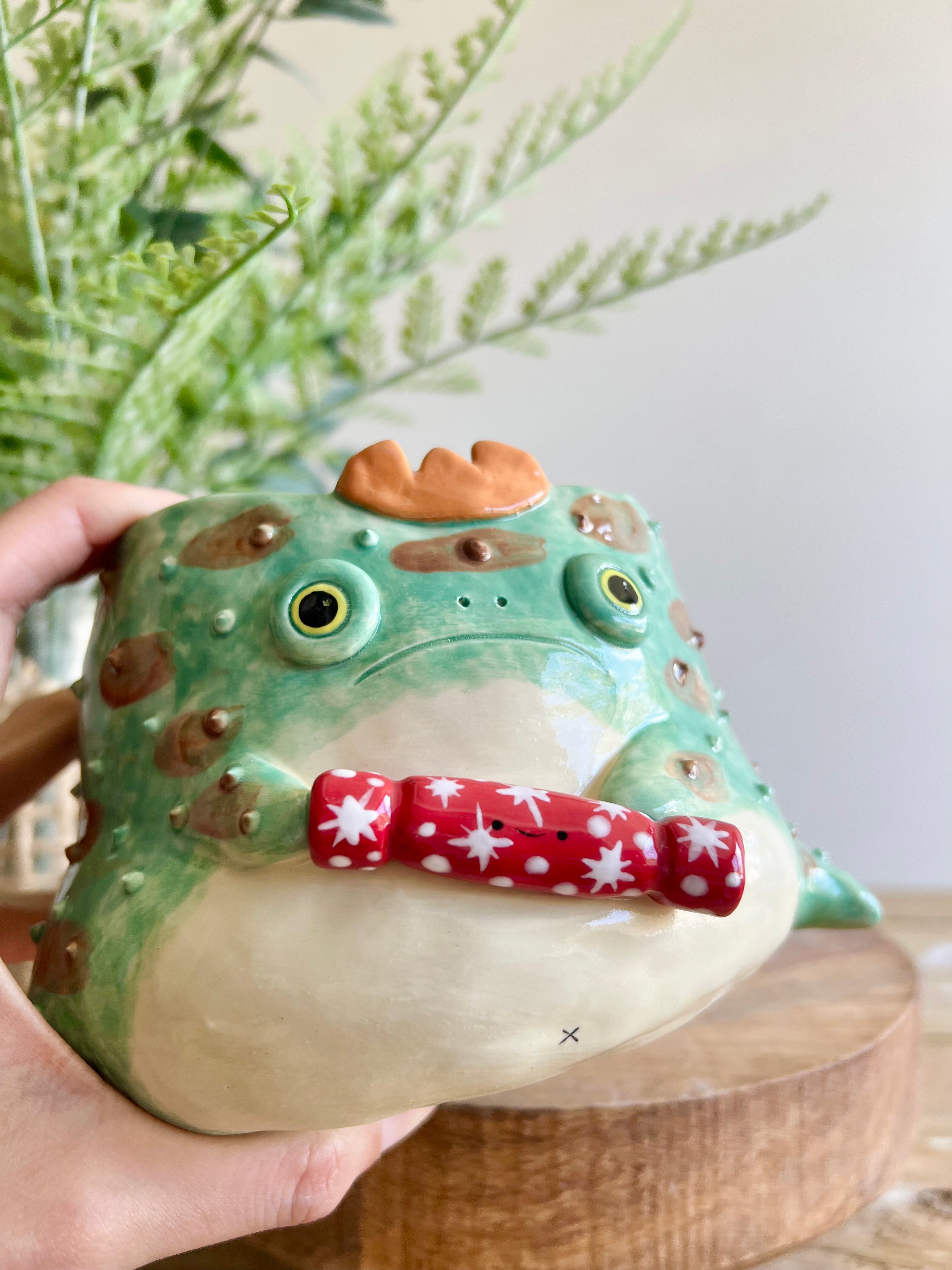 Festive grumpy Froggo planter cracks bon bon with you