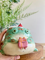 Festive grumpy Froggo planter bearing gift