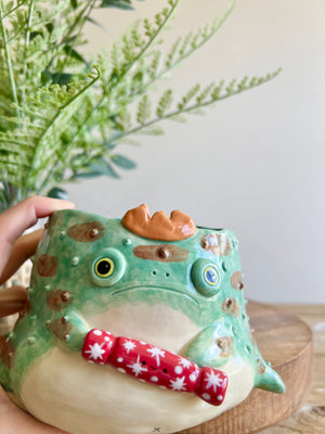 Festive grumpy Froggo planter cracks bon bon with you