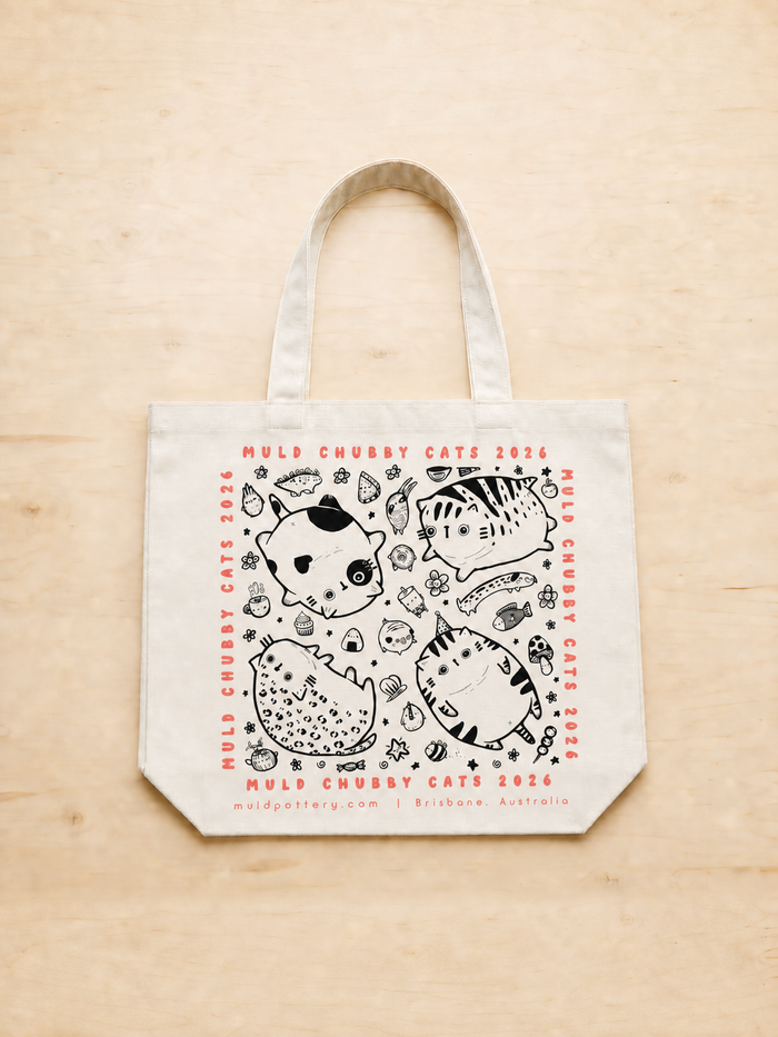 Cream Chubby Cats exhibition tote bag with centred print, portrait flat lay on pale timber